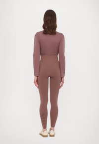Brown long-sleeve top paired with matching high-waisted leggings featuring a subtle logo on the left leg, set against a plain background.
