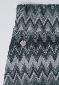 Tissu tricoté avec un motif zigzag vert foncé et gris, avec une petite étiquette métallique ronde portant la mention "Street One".