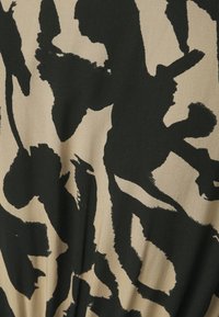 Tissu noir et beige présentant un motif audacieux d'imprimé animal abstrait ; texture douce avec un tombé naturel, conçu pour le confort et la polyvalence.