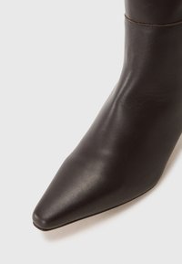 Stivaletto a punta in pelle marrone scuro, caratterizzato da una texture liscia e un design aderente che si restringe alla caviglia. Vista la cucitura.