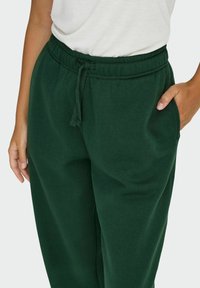 Mørkegrønne sweatpants med taljeelastik og sidelommer, med en blød tekstur og afslappet pasform.