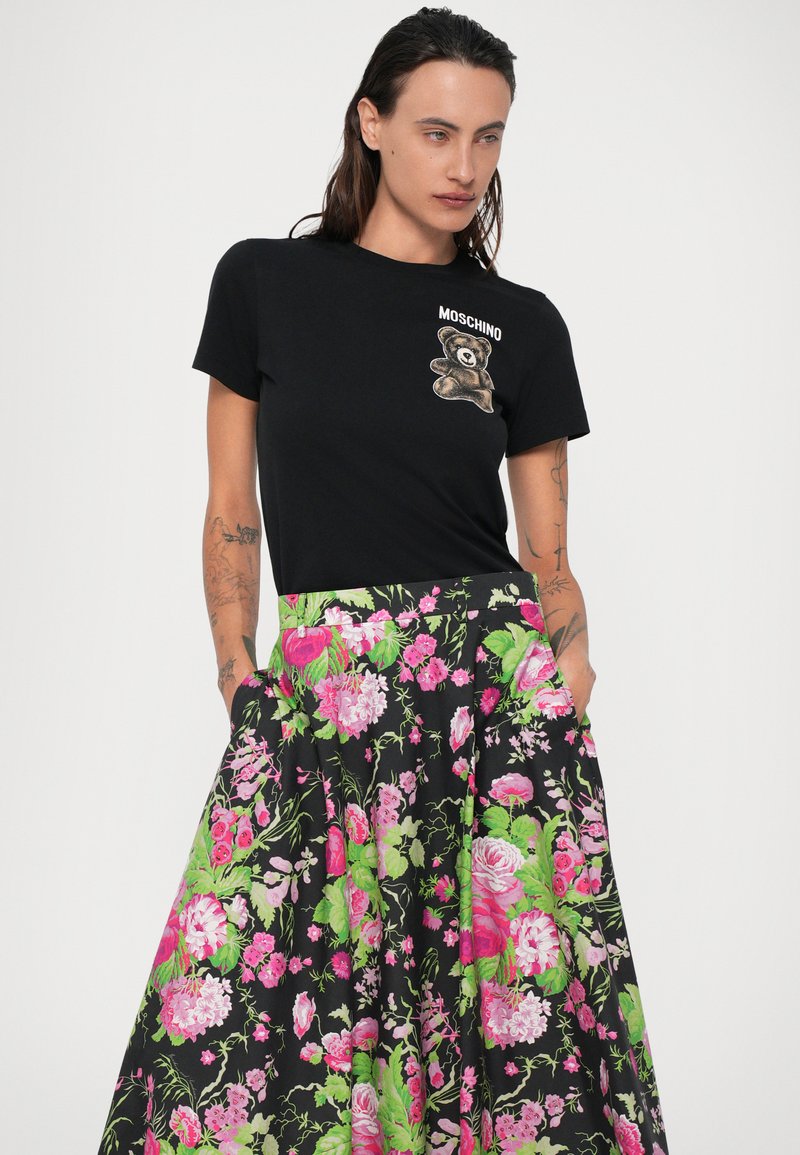 Sort t-shirt med et bjørneprint, parret med en blomsterkjole i sort, pink og grøn. Kjolen har lommer og en tætsiddende talje.