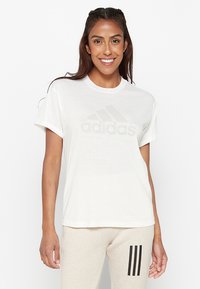 T-shirt bianco in cotone con maniche corte, caratterizzato da un logo Adidas grigio chiaro sul petto. Tessuto morbido e vestibilità rilassata.