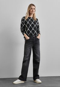 Sort- og hvidmønstret langærmet sweater kombineret med højhvide sorte jeans og hvide sneakers. Blød tekstur, afslappet pasform og vidde ben-design.