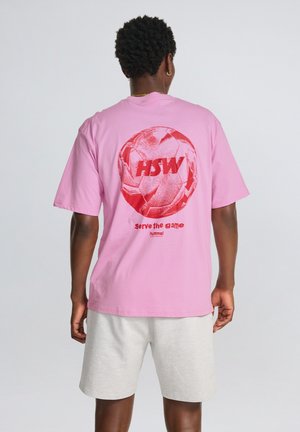 Rosa Baumwoll-T-Shirt mit großem roten Grafik eines Fußballs und dem Text "HSW" sowie "serve the game" auf der Rückseite. Kurze Ärmel.