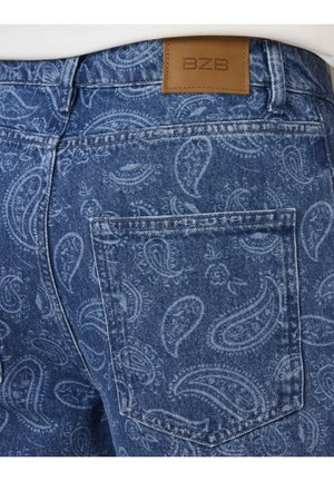 Jean en denim avec motif paisley bleu clair, poche arrière visible et patch en cuir marron marqué BZB à la ceinture.