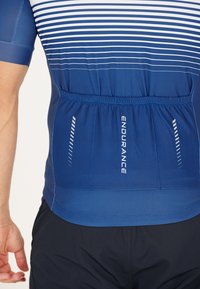 Sininen urheilupaita, jossa on valkoiset vaakaviivat, joustavaa materiaalia, jonka vyötäröllä on kuminauha ja jonka sivussa on teksti "KESTÄVYYS".