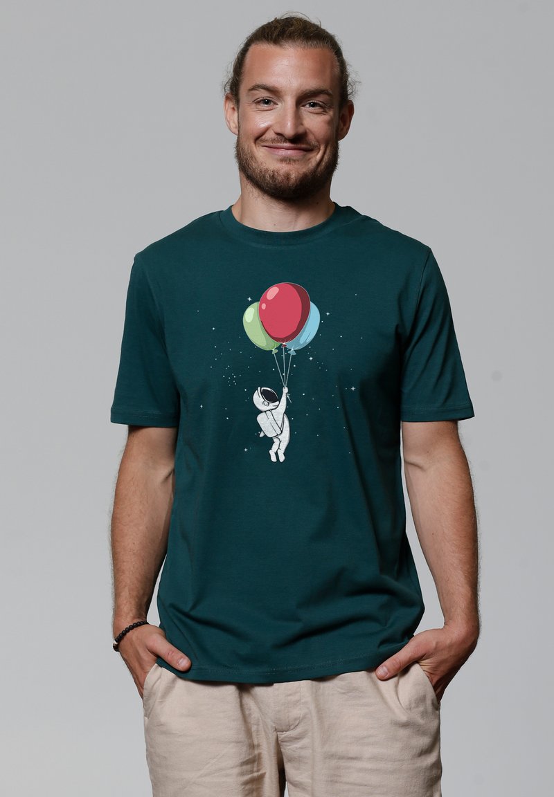 T-shirt en coton teal avec un graphique d'un astronaute tenant trois ballons colorés. Manches courtes et coupe décontractée, design minimaliste.