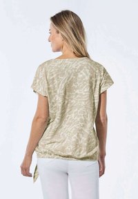 Lichtbeige top met een textuur, luipaardprint patroon, korte mouwen en een gathered zoom. Gecombineerd met witte broek.