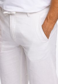 White linen pants featuring a relaxed fit, front pockets, and a drawstring waist. The texture appears lightweight and slightly crinkled.