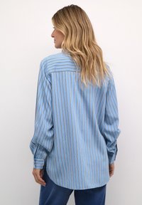 Blue striped long-sleeve shirt with contrasting vertical stripes in gold. Features a relaxed fit, curved hem, and buttoned cuff details.