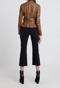 Giacca peplum in pelle marrone, design aderente. Indossata con jeans neri a campana tagliati e stivali neri fino alla caviglia con accenti di anelli in argento.