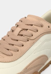 Μπεζ δερμάτινο αθλητικό παπούτσι με κορδόνια, με λευκό δερμάτινο πλαϊνό πάνελ και υφασματικές λεπτομέρειες. Επίπεδα κορδόνια και διακριτική σήμανση στο πλάι.