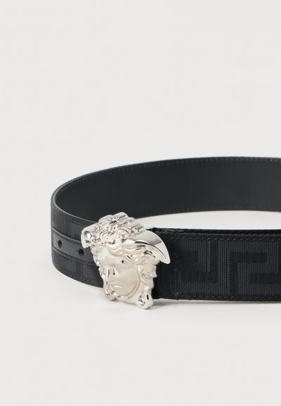 Μαύρη ζώνη με ανάγλυφο υφασμάτινο μοτίβο και αγκράφα με ασημί τόνο σε σχήμα κεφαλής Μέδουσας. Διαθέτει λείες άκρες και ρυθμιζόμενες τρύπες.