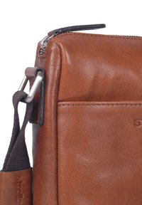 Hnědá kožená taška s texturovaným povrchem, stříbrným zipem a odnímatelným textilním poutkem. Kompaktní, obdélníkový design s nenápadným brandingem.