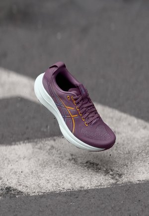 Paarse sportieve schoen met een gestructureerde bovenkant, witte tussenzool, oranje en blauwe accenten en een afgeronde neus. Beschikt over een vetersluiting en een hieltab.