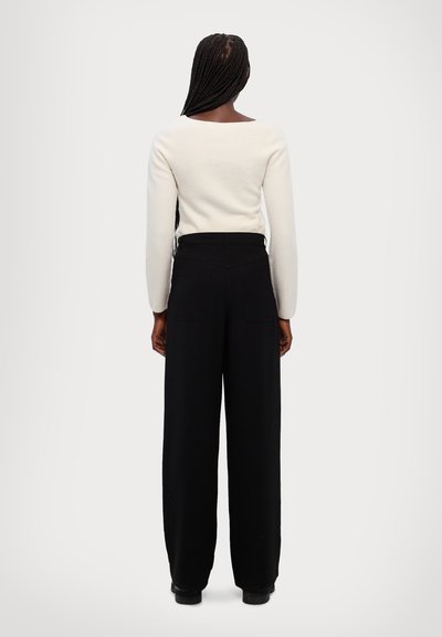 Cream knit top with long sleeves paired with high-waisted black wide-leg trousers featuring back pockets. Neutral color palette.