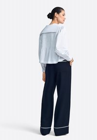 Fehér blúz széles gallérral és ráncolt hátrésszel, hozzá illeszkedő, magas derekú tengerészkék, bő szárú nadrággal, amelynek szegélyén fehér paszpól található.