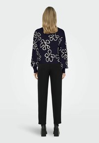 Maglione blu navy con motivi floreali astratti bianchi a contrasto, maniche lunghe, design cropped, abbinato a pantaloni neri e calzature nere spesse.
