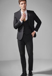 Black suit with a fitted blazer, three-button closure, and matching pants. Textured gold tie and white shirt complete the ensemble.