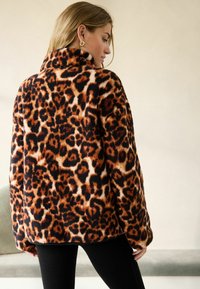 Veste en imprimé léopard avec une texture douce et floue, un col haut et une coupe oversize dans des teintes d'orange, de noir et de crème.