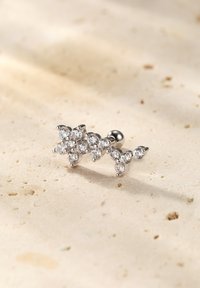 Cuff per orecchio in argento con multiple pietre trasparenti disposte in un motivo floreale, su una superficie di pietra neutra.