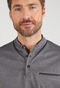 Grijze, knoopsluiting shirt met een Mandarin-kraag, gemaakt van een gestructureerde stof, met een borstzak met een geprinte rand en twee knopen bij de nek.