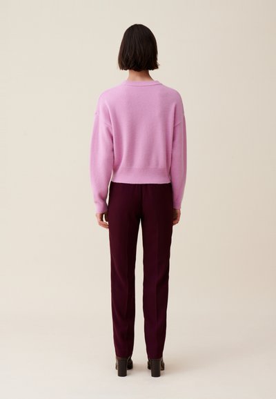 Pull en mélange de laine rose à épaules tombantes, avec un ourlet côtelé, associé à un pantalon bordeaux ajusté et des chaussures à talons blocs. Vue arrière affichée.