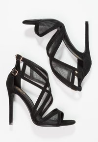 Mustat korkokengät, joissa on yhdistelmä mokkaa ja verkkoa, ristiin menevät hihnat ja kultasävyiset soljet turvallista kiinnitystä varten.