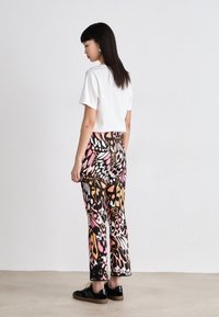 Weißes, kurzes T-Shirt, das mit bunten, gemusterten weiten Hosen kombiniert ist, die rosa, orange und schwarze Schmetterlingsmotive zeigen. Schwarze Sneakers.