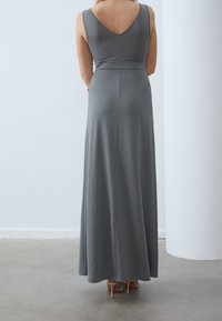 Pitkä, harmaa, hihaton mekko, jossa on V-muotoinen selkäosa, sileä pinta ja vartalonmyötäinen vyötärö, joka laskeutuu leveään helmaan. Yhdistetty korkeakorkoisiin kenkiin.