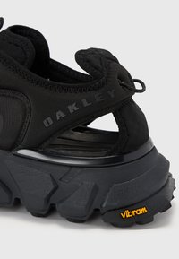 Melni apavi ar teksturētu auduma augšdaļu, ar masīvu zoli, papēdi vilkšanas cilpiņu un dzelteno "Vibram" logotipu uz zoles.