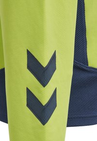 Grønt og marineblåt atletisk stof med et struktureret mønster og et fremtrædende marineblåt chevron-design på ærmet.