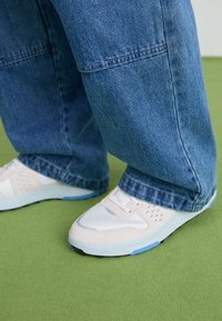 Vita och ljusrosa sneakers med mesh och inslag av blått, matchade med löst sittande mörkblå jeans.