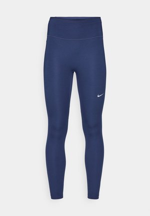 Marineblå leggings med høy midje, laget av elastisk stoff. Har subtil søm og en liten hvit Nike-logo på venstre lår.