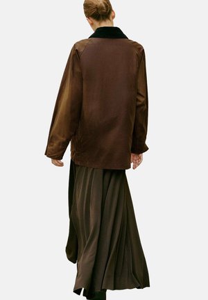 Veste en satin marron avec un col noir, associée à une jupe plissée fluide de couleur marron foncé. Texture lisse, coupe oversize, design mi-long.