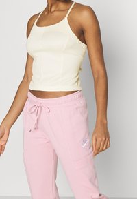 Light yellow cropped tank top with thin straps paired with pink sweatpants featuring a drawstring and Nike logo. Soft fabric and casual fit.