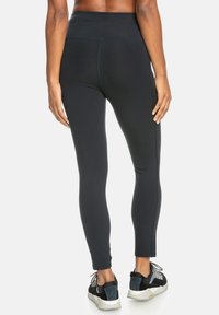 Schwarze Leggings mit hohem Bund, glatter Textur und taillierter Passform, kombiniert mit schwarzen und grauen Sportschuhen mit strukturierten Akzenten.
