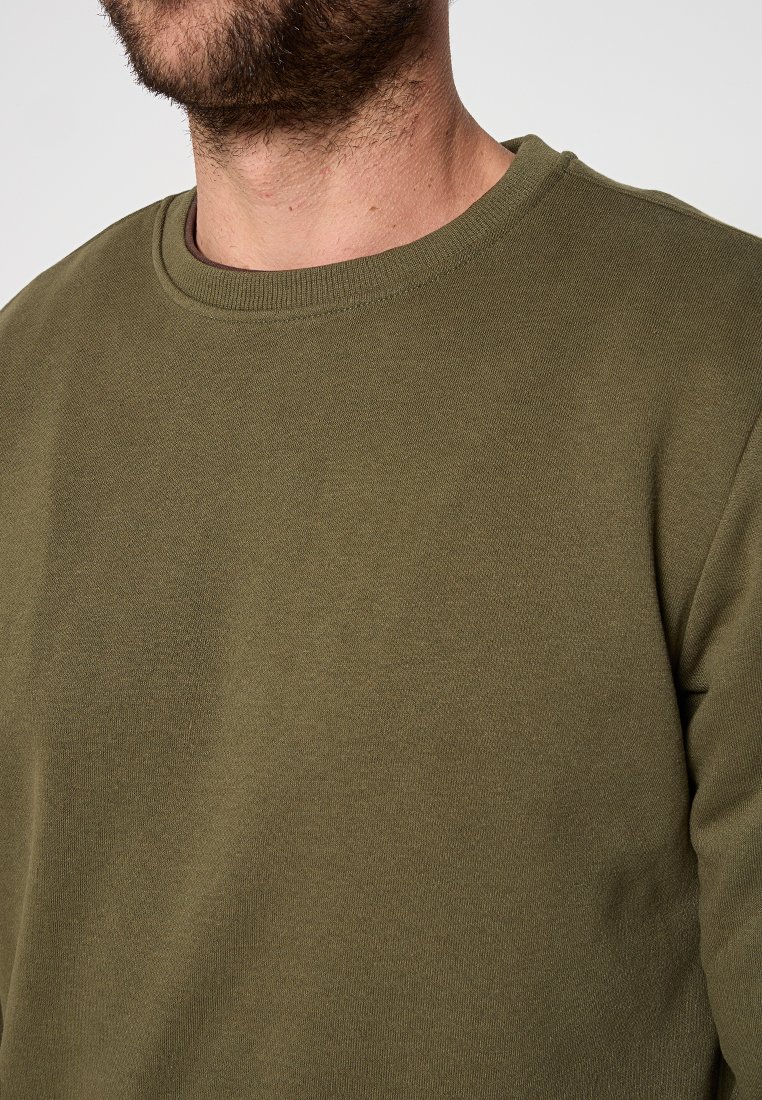 Sweatshirt vert olive avec un col rond, en tissu mélangé coton, et détails de poignets côtelés, présenté de la poitrine vers le haut sur un mannequin.