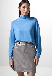 Maglione blu a maniche lunghe con colletto a imbuto abbinato a una mini gonna metallica argento. Il maglione è morbido e la gonna presenta una texture liscia e lucida.