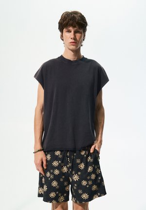 T-shirt sans manches gris foncé avec un col rond, associé à un short noir présentant un léger motif de soleil. Tissu doux et décontracté.