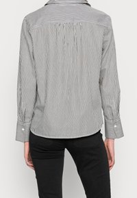 Chemise à rayures noires et blanches avec un empiècement au dos, des manches longues et des poignets boutonnés. Fabriquée en tissu léger avec une coupe décontractée.