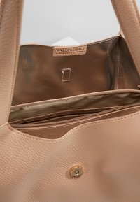 Beige läderhandväska med texturerad yta, med en dragkedjeförsedd innerficka, guldfärgade detaljer och en logotagg inuti.