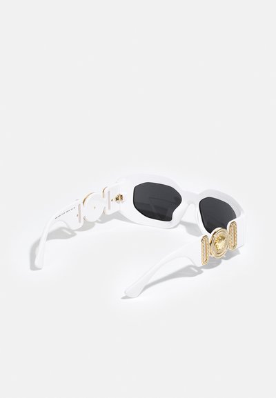 Ochelari de soare albi cu un cadru unghiular, lentile întunecate și un accent de leu auriu pe lateral, având un hardware texturat și un finisaj neted, lucios.