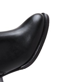 Zwarte leren schoen met een ronde neus en een gladde textuur, met een gestroomlijnd ontwerp en een lichte hak. Geen zichtbare hardware of accenten.