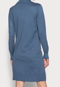 Robe tricotée en bleu muted, avec un col montant, des manches longues, des poignets côtelés et un ourlet légèrement évasé pour un ajustement décontracté.