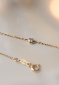 Gold chain bracelet featuring a round bezel-set clear stone, smooth surface, and a secure lobster clasp for closure.