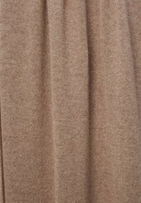 Tissu tricoté beige avec une texture douce, présentant des variations subtiles de couleur et un motif régulier. Idéal pour les vêtements ou le textile d'ameublement.