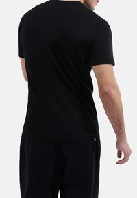 Mężczyzna w zwykłej czarnej koszulce z krótkim rękawem i czarnych spodniach, pokazany od tyłu na tle białego tła.