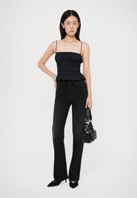 Top peplum negru cu bretele subțiri, asortat cu blugi negri ajustați. Accesoriile includ o geantă mică neagră și pantofi negri cu vârf ascuțit.